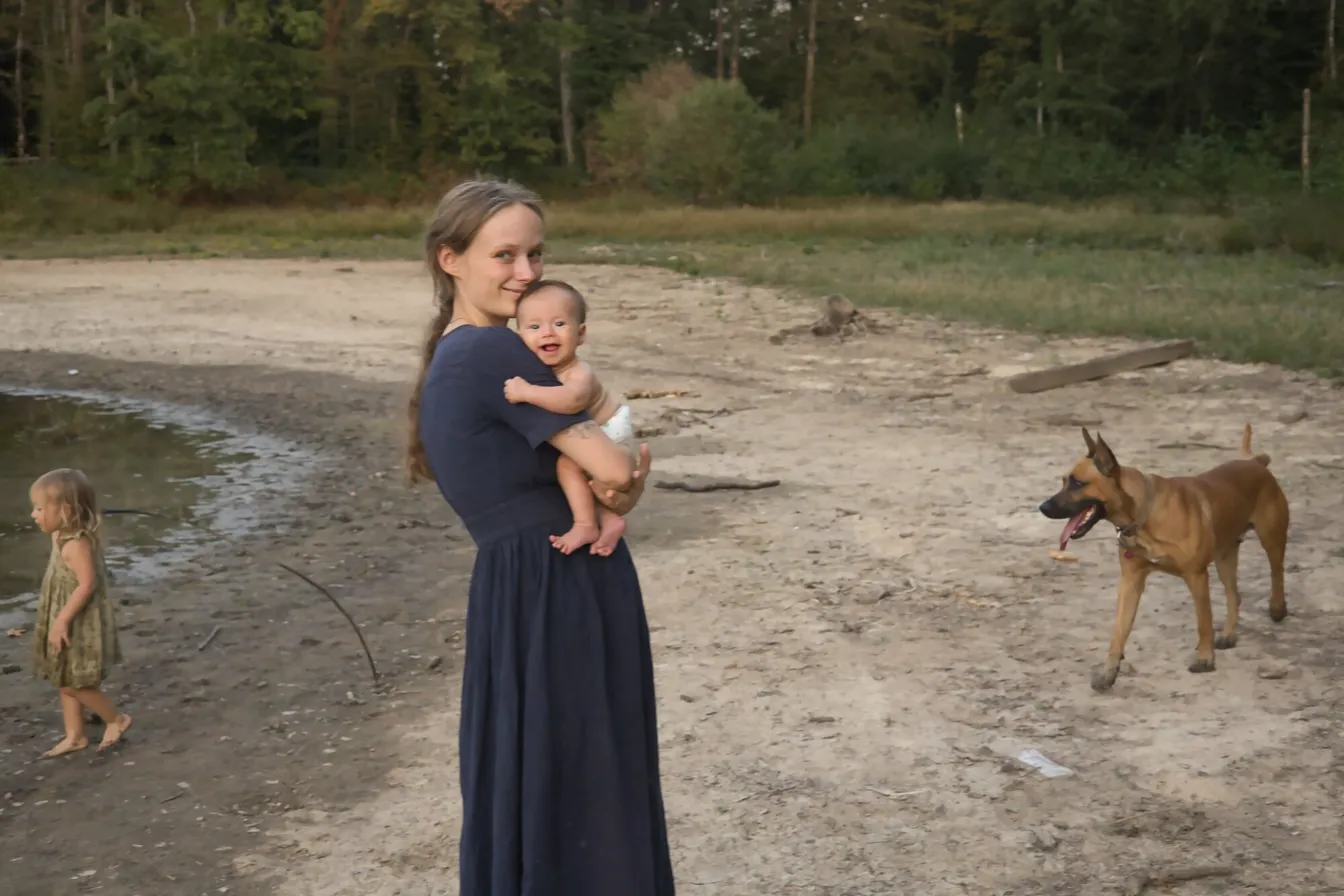 Calypso Bonnefoy au bord d'un étang, son bébé dans les bras, sa fille aßnée et le chien de la famille autour d'elle